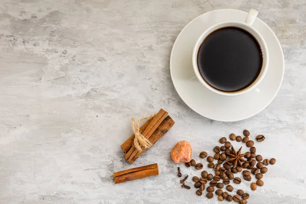 Kahve çekirdeklerinin yanında bir fincan sade kahve, tarçın ve açık arkaplanda bir parça şeker.. 
