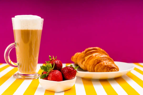 Taze olgun çilekler porselen bir çay tabağında, yanında kruvasan ve İrlanda bardağında kapuçino..