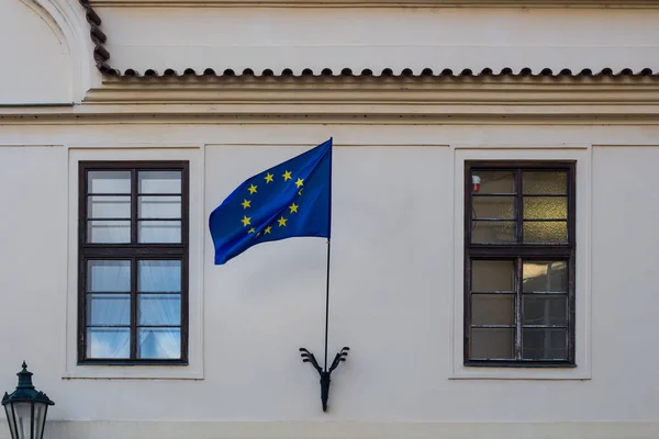 Light color of the facade of a house in Prague. European Union flag waving in the wind. Two windows, one with a reflection of a sky. Street lantern. Prague, Czech republic