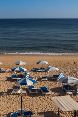 Sandy beach Atlantik Okyanusu sahilinde Armacao da Pera, Algarve, Portekiz. Sandalye ve şemsiye mavi ayrıntıları. Okyanusun sakin su.