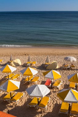 Sandy beach Atlantik Okyanusu sahilinde Armacao da Pera, Algarve, Portekiz. Sandalye ve şemsiye sarı ayrıntıları. Okyanusun sakin su.
