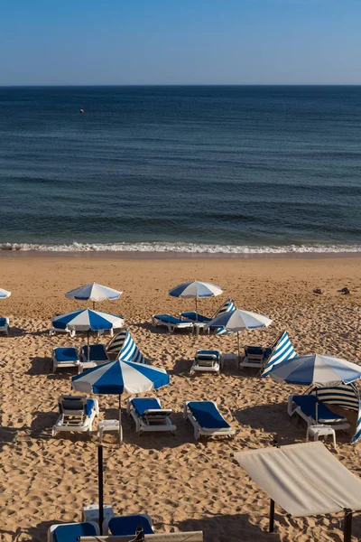 Sandy beach Atlantik Okyanusu sahilinde Armacao da Pera, Algarve, Portekiz. Sandalye ve şemsiye mavi ayrıntıları. Okyanusun sakin su.