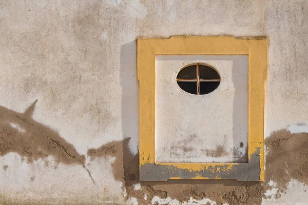 Eski duvar bir evin bir yıpranmış beyaz cephe ve sarı bir çerçeve ile. Oval küçük pencere çerçeve içinde. Armacao de Pera, Algarve, Portekiz.