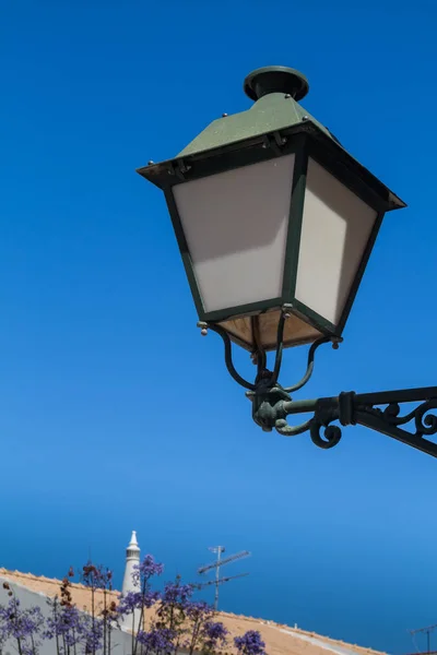 Lantern in a traditional style during the day. Bright clear blue sky. Diagonal line of the city in the background. Estoi, Algarve, Portugal.