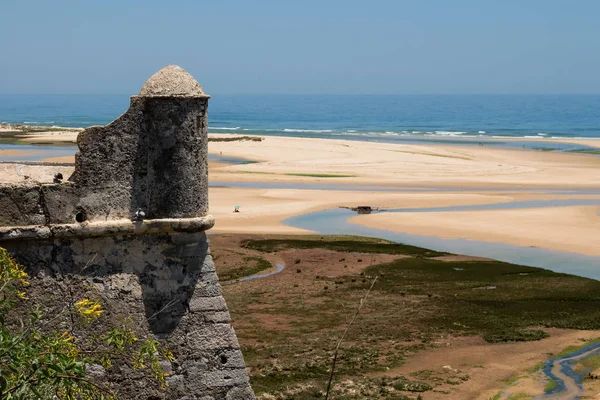 Taştan yapılmış eski kale kule. Su birikintileri ile kumlu bir plaj sonra yüksek gelgit görüntüleyin. Ufuk Atlantik Okyanusu'nun. Mavi gökyüzü. Cacela Velha, Algarve, Portekiz.