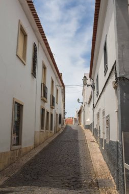 Tepeye beyaz evler astarlı ve cobblestones tarafından döşeli dar sokak. Geleneksel fenerler. Çatı kiremitleri hattı. Bulutlu gökyüzü. Lagos, Algarve, Portekiz