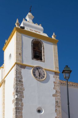Kule Igreja Matriz de Alvor - Portekizce şehir kilisede. Beyaz cephe sarı ayrıntılarla. Gruuthuse Müzesi ve saat. Fener binanın yanında. Parlak mavi gökyüzü. Alvor, Algarve, Portekiz.