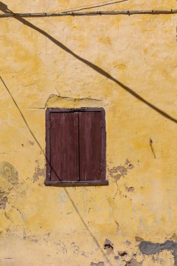 Sarı renk bir evde El Jadida, Fas ve yıpranmış cephe. Ahşap kahverengi kapalı çekim pencere. Kablolar sokakta gölge hatları.