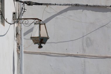 Beyaz bir cephe ile iki bina köşesine. Sokak lambası - fener duvarda aşağı tarafı yukarı yüklü. Pek çok kablo ve onların gölgeler. Rabat, Morocco.