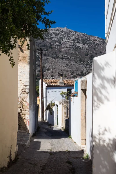 Narrow weathered road and pavement. Mostly white facades  of the houses. Blue sky. High rocky mountain in the background. Traditional village Archanes in the mountains  Crete, Greece.