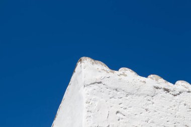 Beyaz bir kaba cephe ve çatı dalgalı bir kenarla ile eski bir ev köşesinde. Parlak mavi gökyüzü. Geleneksel köy Archanes, Crete, Yunanistan.