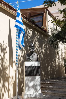 Bir keşiş Afthonios Dretakis, heykeli kim Osmanlılar karşı fough. Yunan bayrağı yanındaki kutup bir haç ile. Gölgeler, ağaç ve bir duvar, bir bina. Archanes, Crete, Yunanistan.