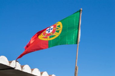 Basit bir ahşap direk bir rüzgarda Portekiz bayrağı. Bir çatı kiremit ile parçası. Açık parlak mavi gökyüzü. Alvor, Algarve, Portekiz.