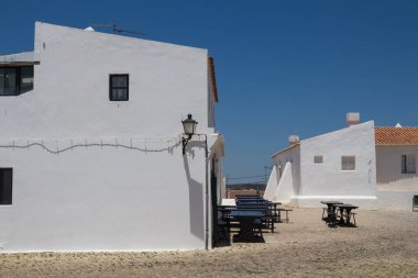 Beyaz duvarları ve eski bir kırmızı kiremit çatı. Kare cobblestones tarafından döşeli. Fener üstünde belgili tanımlık köşe, kablonun gölgesi. Boş tablolar kapalı bir restoran. Cacela Velha, Algarve, Portekiz