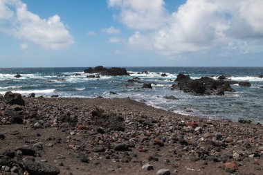 Neredeyse siyah kayalar Atlantik Okyanusu kıyısında keskin. Küçük dalgalar. Ufuk ve mavi gökyüzü bulutlu. Ada Sao Miguel, Azor Adaları, Portekiz.