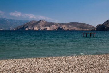 Seaside Adriyatik Denizi. Plaj kum ile kaplı ve küçük taşlar. Bay sakin su. Dağlar içinde belgili tanımlık geçmiş. Bulut ile mavi gökyüzü. Baska, Island Krk, Hırvatistan.