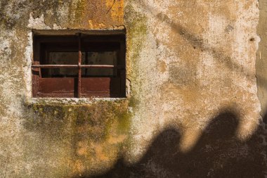 Bir kahverengi kare ve ızgara ile küçük pencere. Yapılandırılmış eski duvar, güneş ışığı ile başka bir evin dalgalı bir gölge tarafından aydınlanmış. Vrbnik, Island Krk, Hırvatistan.