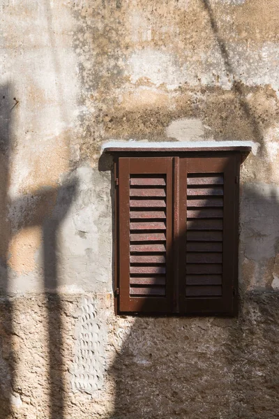 Structured old wall with a shadow of another house. Window with a brown shutter.  Historical city Vrbnik, island Krk, Croatia.