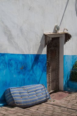 Bir evin bir kısmı tarafından parlak mavi renk boyalı duvar. Süslü kapı. Eski yatak duvar yanında. Sokak cobblestones tarafından döşeli. Kasbah de Oudaias, Rabat, Morocco.