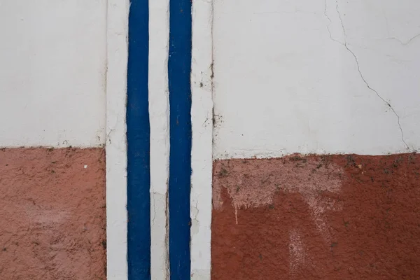 Red and white painted house with a vertical blue and white lines. Older facade. Faro, Portugal.