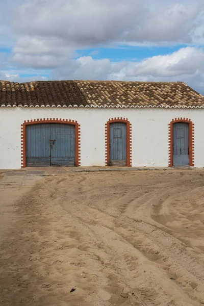 Mavi ahşap kapı ve çerçeveler ile binanın beyaz cephe turuncu tuğla yaptı. Çok renkli kiremit. Sandy yol. Bulutlu sonbahar gökyüzü. Tavira, Praia do Barril, Portekiz.