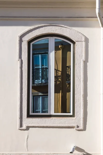 Perfectly clean window with a frame and an arch, reflecting window and wall of another house. City centre of Lisbon, Portugal.