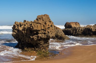 Plaj kıyısında küçük taşlarla. Yabani su dalgaları ile Atlas Okyanusu. Açık mavi gökyüzü. Ufuk içinde belgili tanımlık geçmiş. Beddouza beach, Fas.