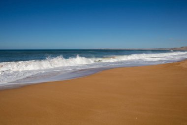 Sonbahar Beach temiz koyu sarı kum. Atlantik Okyanusu su köpüklü dalgalar ile derin mavi rengi. Ufuk içinde belgili tanımlık geçmiş. Açık mavi gökyüzü. Lalla Fatna beach (Safi). Fas.