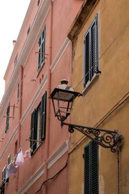 Pencereli ve panjurlu renkli evler. Duvarda geleneksel bir fener var. Çamaşır sırası. Bulutlu bir gün. Alghero şehir merkezi, Sardinya, İtalya.