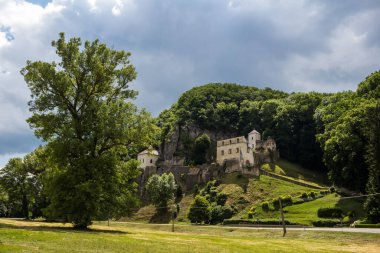 Ağaçlarla çevrili bir dağda inşa edilen manastırın Gotik binası. Baharda bulutlu bir gökyüzü. Velka Skalka, Slovakya.