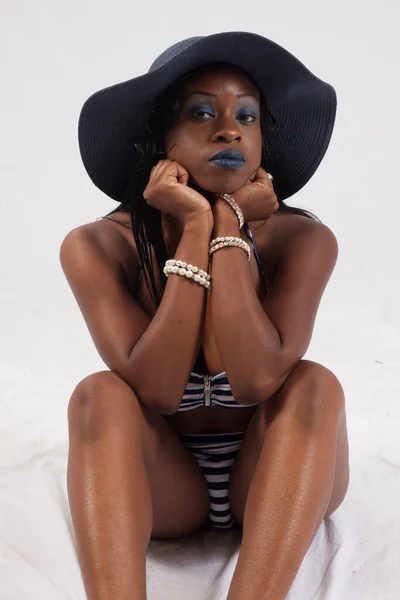 Pretty Black woman in a swim suit and hat, sitting on the floor