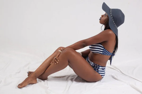 Pretty Black woman in a swim suit and hat, sitting on the floor