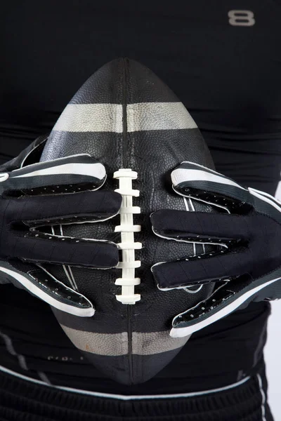 Hands in a glove holding a black American Football,
