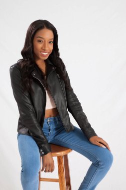 Siyah deri ceketli mutlu kadın, taburede oturuyor ve gülümsüyor.