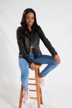 Siyah deri ceketli mutlu kadın, taburede oturuyor ve gülümsüyor.