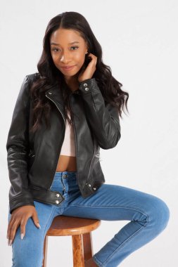 Siyah deri ceketli mutlu kadın, taburede oturuyor ve gülümsüyor.