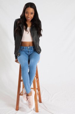 Siyah deri ceketli mutlu kadın, taburede oturuyor ve gülümsüyor.