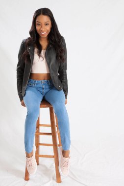 Siyah deri ceketli mutlu kadın, taburede oturuyor ve gülümsüyor.