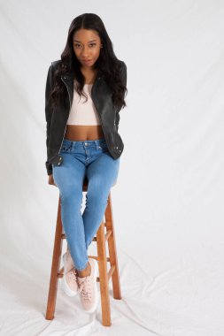 Siyah deri ceketli mutlu kadın, taburede oturuyor ve gülümsüyor.