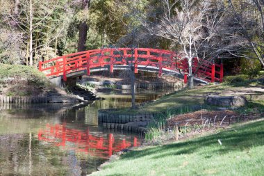 Göle yansıyan kırmızı kemerli bir köprü.