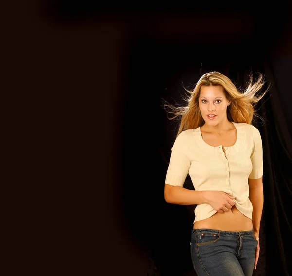 Beautiful woman model posing in simple elegant tan top and jeans in the studio - isolated on solid black copy space background - short sleeves - button  front - modern comfort - long blonde wind blown blonde hair - catalogue pose simple look