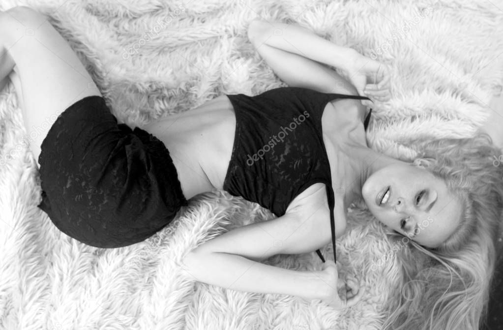Adorable Long Hair Blonde posing in bedroom studio setting laying down on fuzzy  fur as copy space background, Landscape monochromatic monochrome in simple comfortable sleepwear