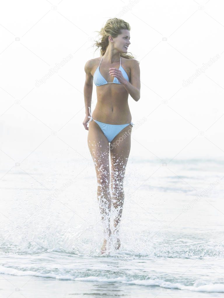 Blonde in blue skimpy bikini running thru water splashing and having fun