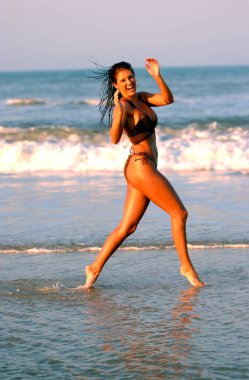 Gün batımı aydınlatma - güneş sırılsıklam trim atletik çalıştıran ve dans oynamaya uygun ünlü Model Wendy Meece - Atlantik Okyanusu Daytona Beach Florida deniz tarafında kum ve kaya, rahat bir altın ışık mavi sıcak dalgaları ile akşam