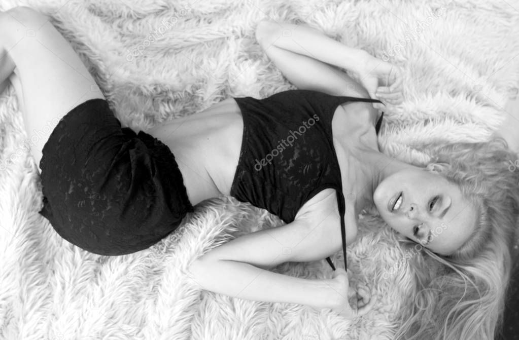 Adorable Long Hair Blonde posing in bedroom studio setting laying down on fuzzy fur as copy space background, Landscape monochromatic monochrome in simple comfortable sleepwear