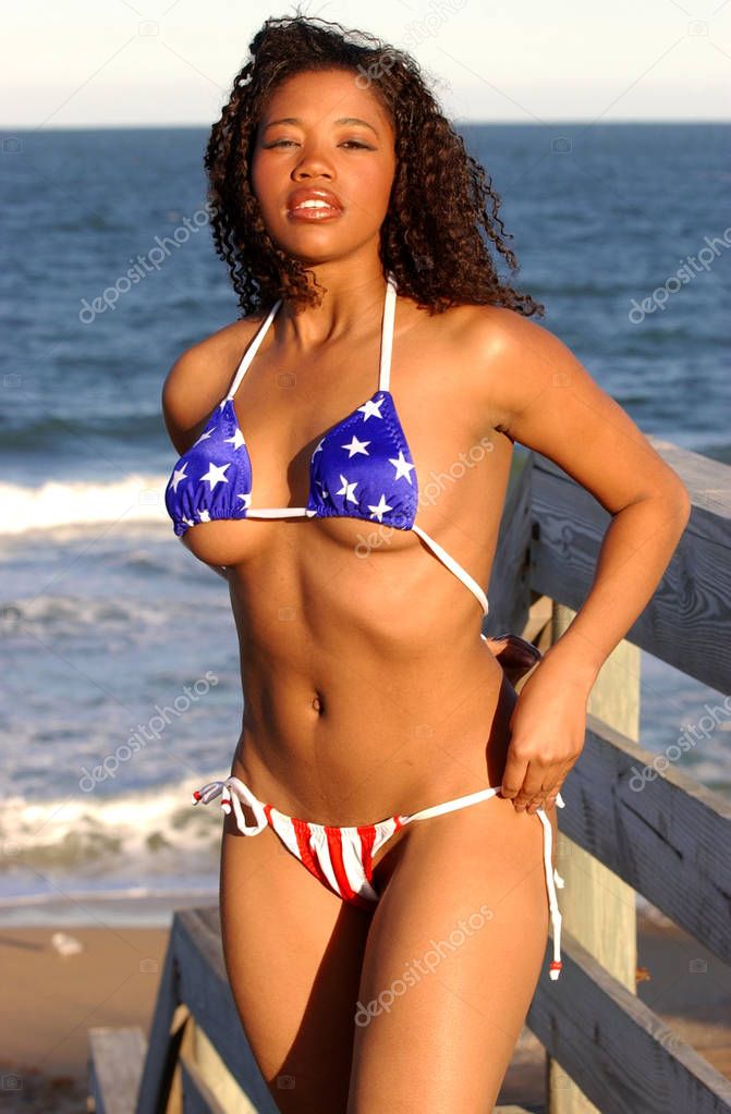 Adorable brunette in skimpy red white and blue string bikini with stars and strips on very pretty sultry body smiling enchanting bewitching lovely lady captivating engaging endearing eyes standing sleek slim hour glass shape natural perky suggestive