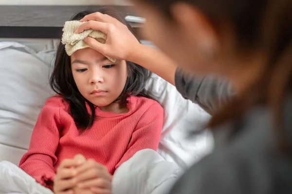 Asian mother take cool towel for reduce high fever on sick girl forehead on bed at morning time, Selective focus, Healthy and infection concept