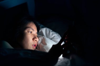 Karanlık yatak odasında cep telefonu kullanan Asyalı kadın uykusuzluktan uyuyamıyor..