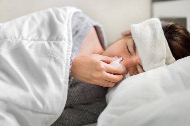 Hasta Asyalı kadın ateşle savaşıyor ve yatak odasındaki yatağa hapşırıyor. Tıbbi ve sağlık konsepti, seçici odaklanma..