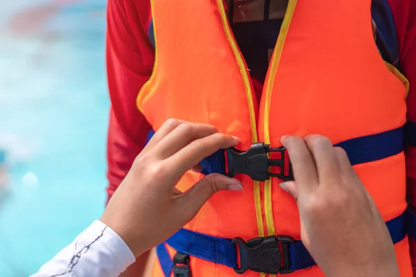 Asyalı anne, yüzme havuzunda oynamadan önce oğlunun can yeleği giymesine yardım ediyor..